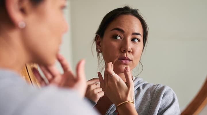 Woman looking in mirror at aging skin