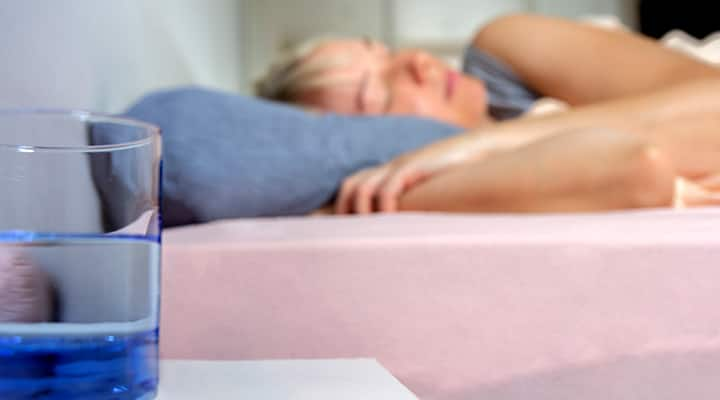 Glass of water sitting on nightstand while woman is asleep in bed