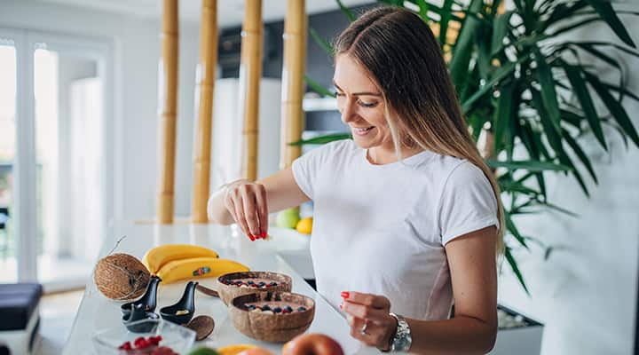 Woman adding a vegan supplement to varied fruit bowl to avoid nutrient deficiencies