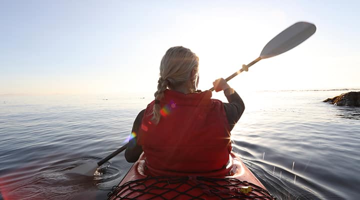 Woman padding a kayak toward a setting sun