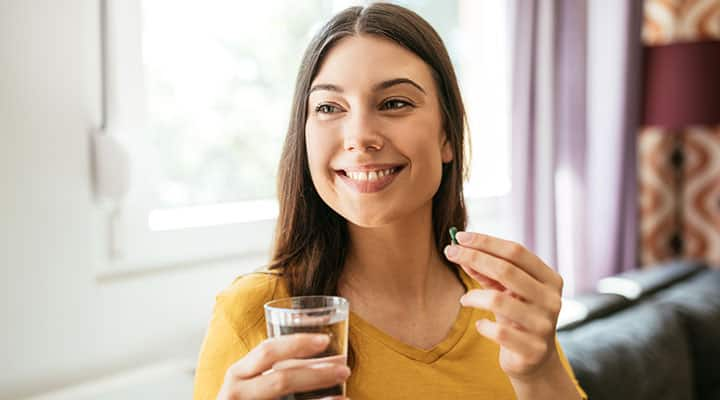 Woman taking DHEA supplement with a glass of water